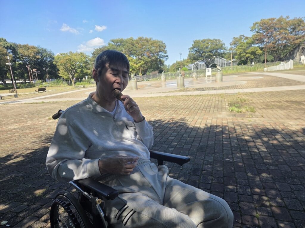 青空の下、相模原麻溝公園の噴水広場で車椅子に座ってアイスを味わう利用者様
