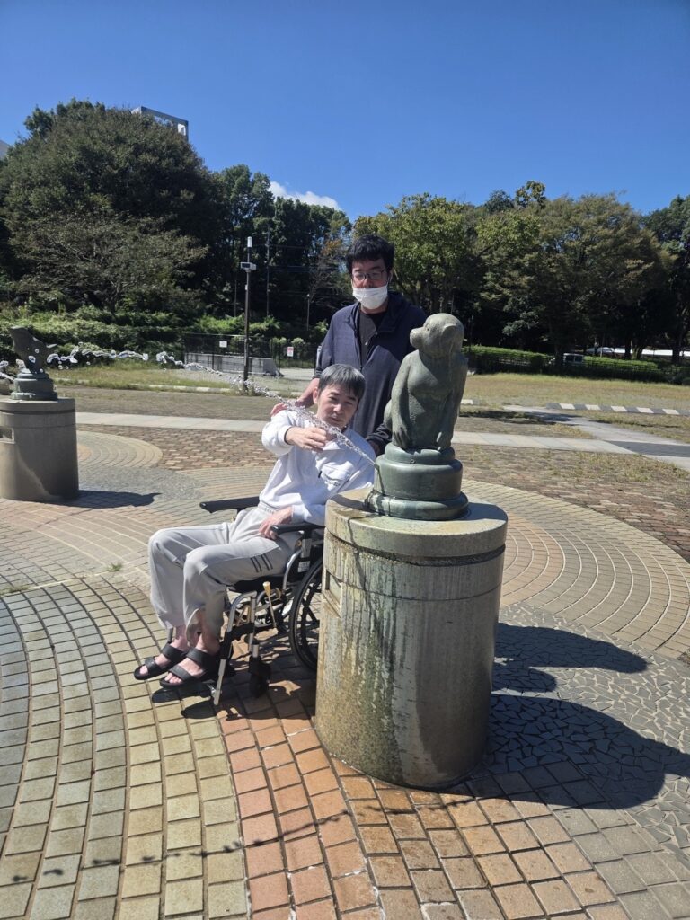 相模原麻溝公園の噴水広場で、おさるの像の噴水の水に手を伸ばす車椅子の利用者様とスタッフ